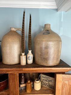 two large jugs are sitting on top of a wooden shelf next to other items