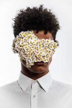 a man with flowers on his face and shirt over his eyes, looking at the camera