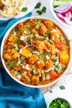 a bowl filled with chicken curry next to other bowls of vegetables and pita bread