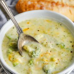 a white bowl filled with broccoli soup next to bread