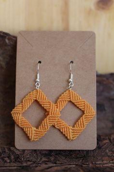 the earrings are made out of woven material and have square shaped beads on them,