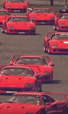 a group of red sports cars driving down a race track with other cars behind them