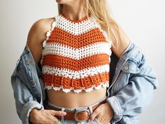 a woman wearing an orange and white crochet crop top with her hands in her pockets