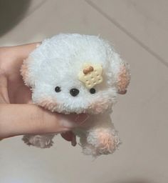 a hand holding a small white teddy bear