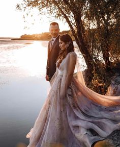 a man and woman standing next to each other in front of a body of water