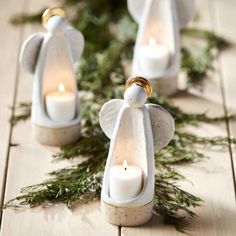 three white angel candles are sitting on a table with greenery and pine cones around them