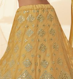 COLOR : Pale Mustard FABRIC : Top (Blouse) - Organza, Bottom (Lehenga) - Organza, Dupatta - Soft Net WORK : Heavy Silk Thread Embroidery, Heavy Foil Mirror Work, Floral Motifs, Lace Border OCCASION : Wedding, Reception, Sangeet, Engagement READY-TO-WEAR : NoSTITCHING : Available as semi-stitched fabric, can be stitched using standard size option (+$30). Note: There might be a slight color variation due to lighting and flash used during photoshoot. The bright shade seen is the best closer view of Festival Georgette Sets With Motifs, Fitted Embroidered Fabric With Motifs For Reception, Chanderi Sets With Motifs For Reception, Unstitched Lehenga With Motifs For Reception, Festive Georgette Lehenga With Motifs, Festive Floor-length Lehenga With Motifs, Fitted Georgette Lehenga With Motifs, Fitted Lehenga With Mirror Work In Art Silk, Diwali Kundan Lehenga With Motifs