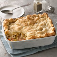 a chicken pot pie in a white dish on a blue towel next to silverware