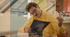 a man sitting at a table with a book in front of him and reading it