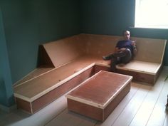 a man sitting on top of a wooden bench in a living room next to a window