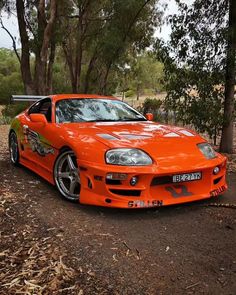 an orange sports car parked on the side of a dirt road in front of trees