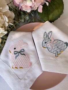 two napkins with embroidered rabbits on them next to some flowers and pink hydrant