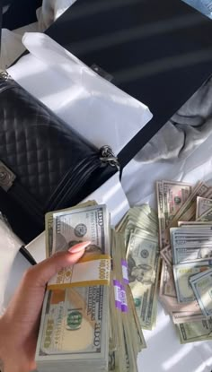 a person holding money in front of a black purse on top of a white table