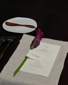 a purple flower sitting on top of a table next to a white plate and utensils