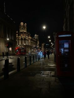 a city street at night with people walking on the sidewalk and a red phone booth in the foreground