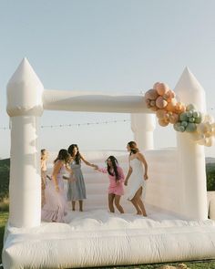 a group of women standing on top of a white inflatable arch with balloons