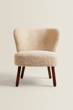 an upholstered chair with wooden legs and a white sheepskin seat cover on it