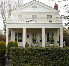 a white house with two balconies on the front and second story, surrounded by hedges