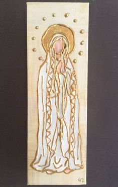 a wooden plaque with an image of the virgin mary in white and gold on it