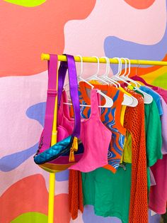 colorful clothing hanging on a rack in front of a painted wall