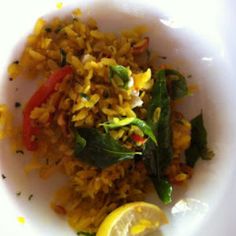 a white plate topped with rice and veggies next to a slice of lemon