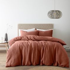 a bed with an orange comforter on top of it in a room next to a brick wall