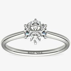 a white gold engagement ring with a round brilliant cut diamond in the center and an inscription on the side