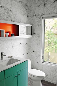 a white toilet sitting next to a sink in a bathroom under a window with an orange wallpaper