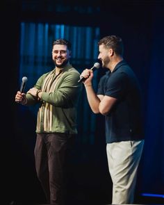 two men standing on stage one holding a microphone and the other singing into a microphone