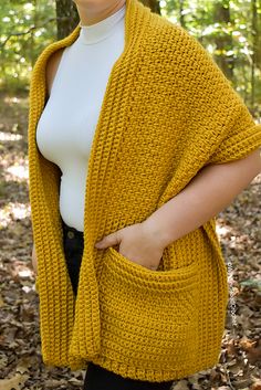 a woman standing in the woods wearing a yellow knitted cardigan