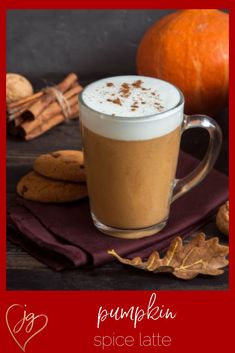 pumpkin spice latte in a glass mug surrounded by fall leaves, cinnamon and an orange