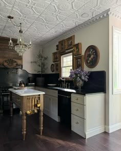 Our Modern Victorian kitchen stills📸 I hope y’all can appreciate the details in the space…the @americantinceilings tiles, the Nero Mist granite counters and tall backsplash with an ogee edge from @graniteworksstone , the antique Italian chandelier, the gorgeous custom dairy table island made by @clevelandcarpentry , the antique floral oil paintings I’ve been collecting , the 1800’s bed frame turned hood vent , the glass bifold pantry with brass @signaturehw Cremone bolts—it all came together ... Victorian Home Kitchen, Modern Victorian Kitchen, Modern Victorian Home, Victorian Home Renovation, Kitchen Victorian, Kitchen Elements, Hood Vent, Victorian Kitchen