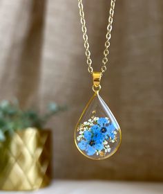 a blue flower in a tear shaped glass pendant hangs from a gold plated chain