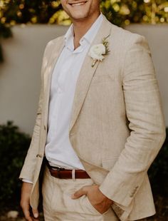 a man in a tan suit with a white flower on his lapel is smiling at the camera