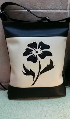 a black and white purse with a flower on the front is sitting against a wall