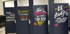 three blue stalls with colorful lettering on them in a public bathroom stall, one has a black toilet and the other is white