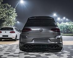 two cars parked in front of each other on a checkered tile parking lot at night