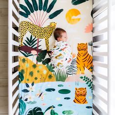 a baby sleeping in a crib next to a wall with jungle animals on it