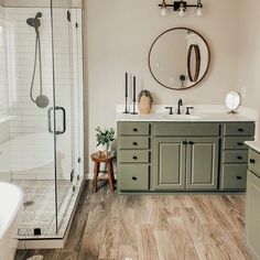 a bathroom with wood flooring and green cabinetry in the shower area, along with a white bathtub