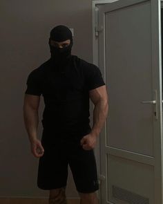 a man wearing a black mask standing in front of a door with his hands on his hips