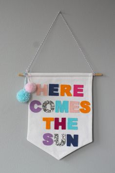 there comes the sun banner hanging on a wall with pom - poms attached to it