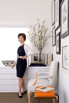 a woman standing in the corner of a room with white furniture and pictures on the wall