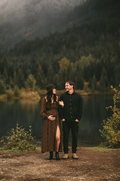 a man and woman standing next to each other in front of a lake