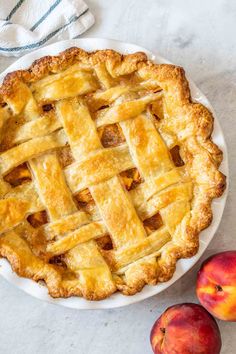 an apple pie on a white plate next to two peaches