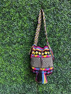 Discover the vibrant fusion of tradition and style with this eye-catching Wayuu mochila, an exquisite piece of artisanry that showcases about a week's dedication from a skilled Wayuu craftswoman in La Guajira, Colombia. This 100% handmade cross body treasure boasts a striking geometric pattern in vivid colors: jet black, pristine white, rich magenta, deep blue, and lively yellow, creating a bold visual statement. Constructed with a resilient double thread crochet technique, this geometric bag is Artisan Multicolor Bucket Bag For Daily Use, Artisan Multicolor Bucket Bag With Adjustable Strap, Traditional Multicolor Bucket Bag With Adjustable Strap, Artisan Multicolor Shoulder Bag With Adjustable Strap, Artisan Multicolor Bag With Adjustable Strap, Artisan Bag With Adjustable Strap For Festival, Artisan Festival Bag With Adjustable Strap, Multicolor Woven Bucket Bag As Gift, Multicolor Woven Bucket Bag Gift