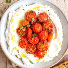 a bowl filled with mashed potatoes and tomatoes on top of a table next to a slice of bread