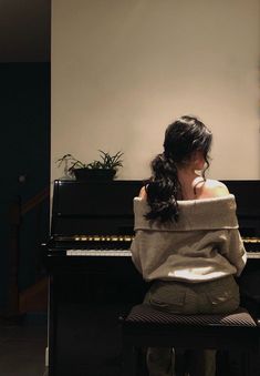 a woman sitting at a piano in front of a potted plant