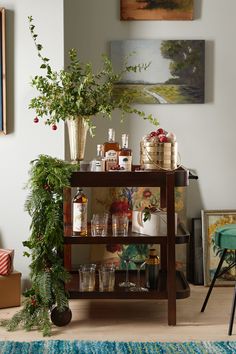 a bar cart filled with bottles and glasses on top of a wooden table next to a potted plant