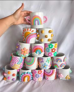 a stack of coffee cups with rainbows and flowers painted on the outside, in front of a white background