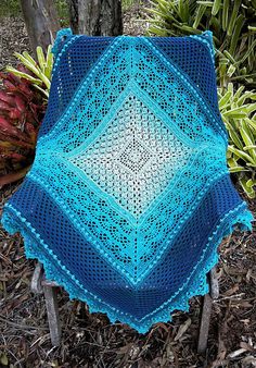 a blue crocheted blanket sitting on top of a wooden chair next to a tree